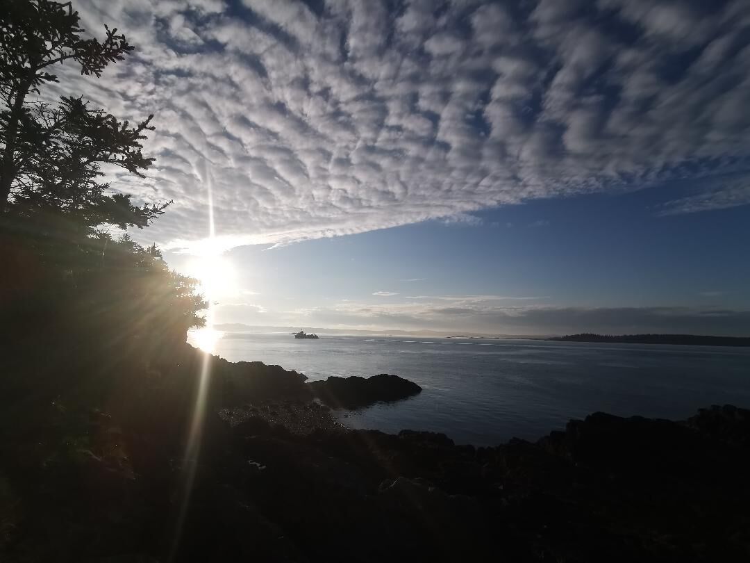 A coastal sunset with the sun low on the horizon, casting rays through the clouds.