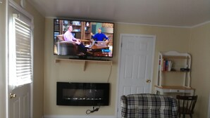 A living room with a television mounted on the wall, a plaid armchair, and a wooden floor.