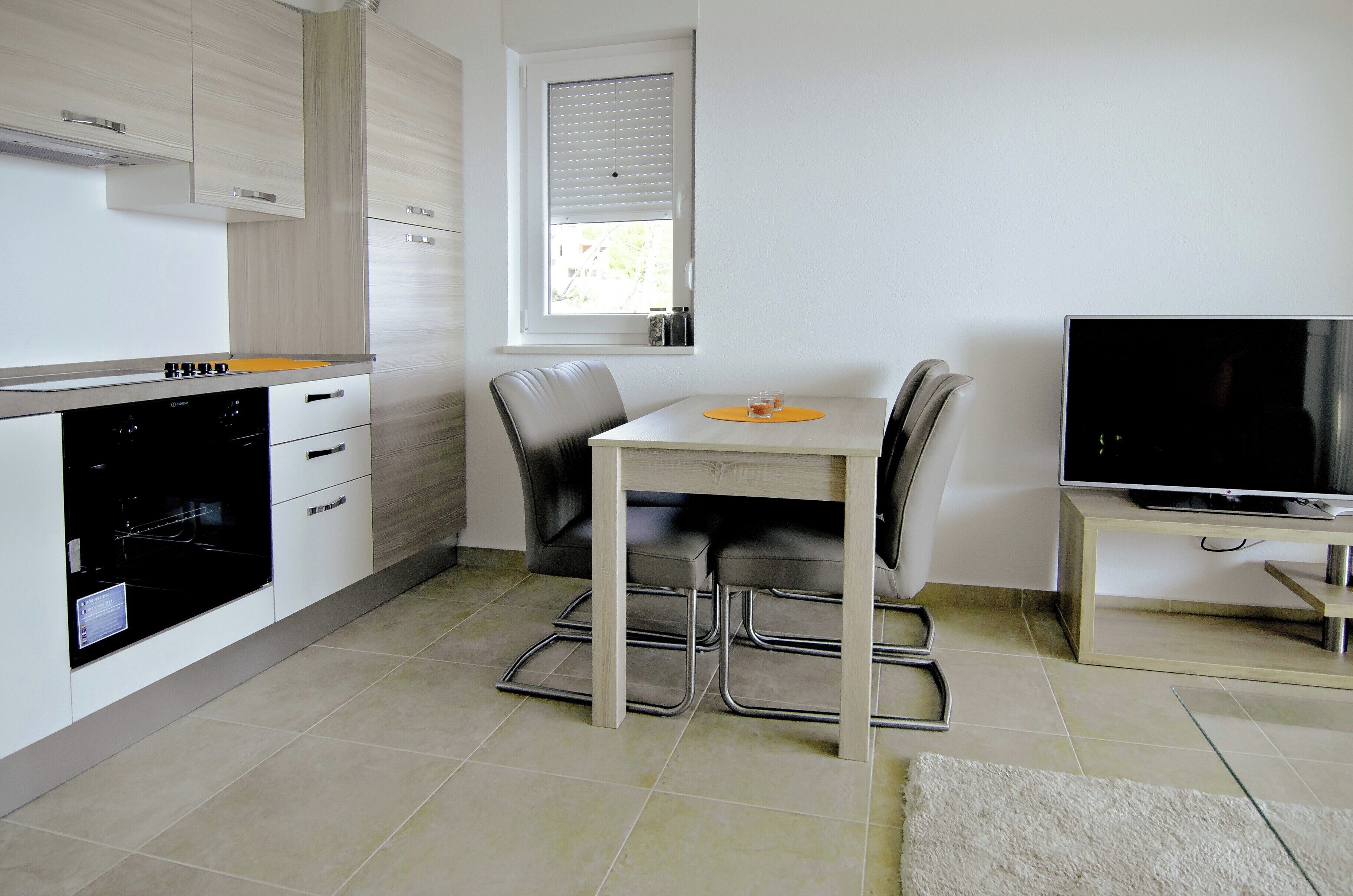 Une cuisine moderne avec une table à manger, des chaises, un four encastré et un téléviseur posé sur un meuble.