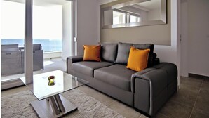 Un salon moderne avec un canapé gris, deux coussins orange, une table basse en verre et un grand miroir au mur.