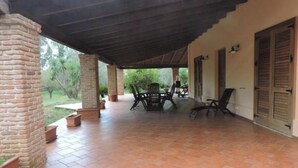 Un patio couvert avec une colonne en briques, une table avec des chaises et une porte avec des volets.
