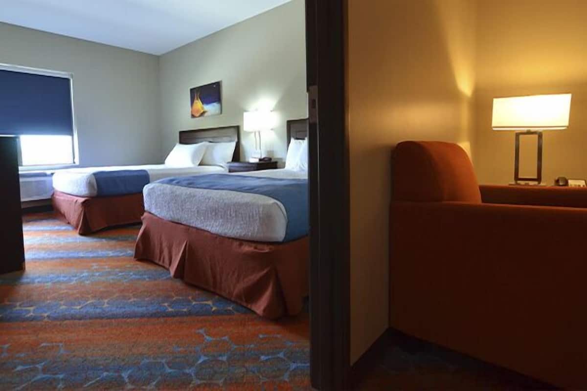 Two beds with matching headboards, a flat-screen TV, and a desk with a lamp.