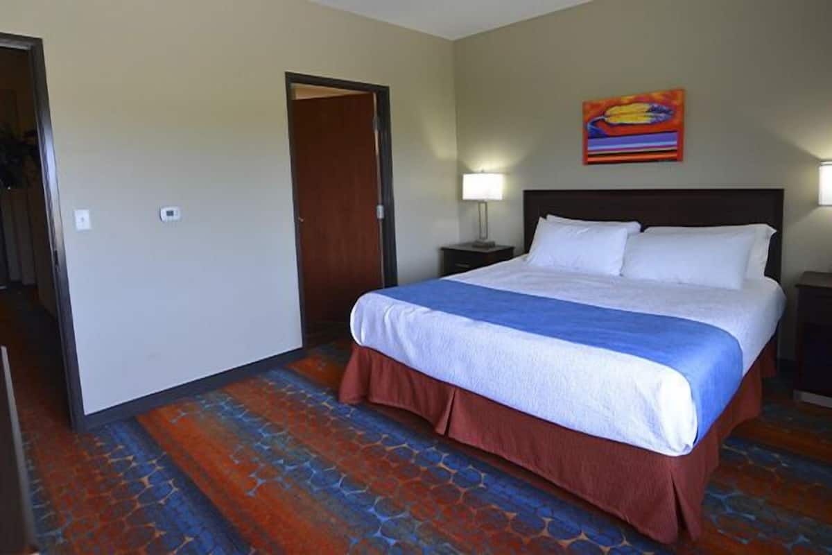 Relax in a spacious room with a large bed, a painting above, and a door leading to another area.
