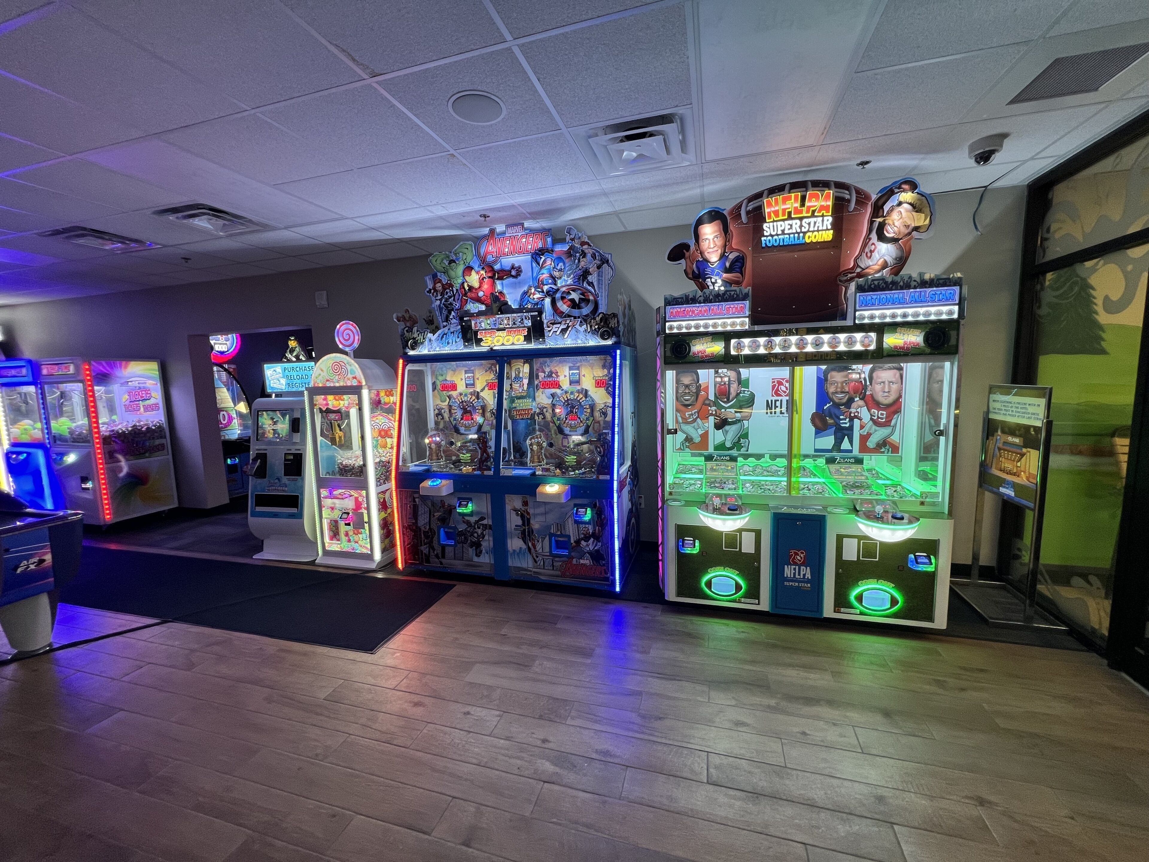 A row of arcade machines with various themes, including Marvel Avengers and NFLPA Super Star Football Coins.