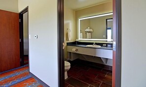 A hotel bathroom with a toilet, sink, and mirror. - 7Clans Hotel & Resort (Newkirk)