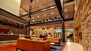 A spacious lobby with a high ceiling, a reception desk, seating area, and a visible staircase leading to an upper level. - 7Clans Hotel & Resort (Newkirk)