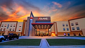 A hotel entrance with a '7 CLANS' sign, a covered entrance area, and a parking lot with a black SUV. - 7Clans Hotel & Resort (Newkirk)