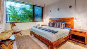 Un dormitorio moderno con una cama grande, cabecero de madera y vistas a zonas verdes a través de un ventanal.