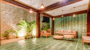 Un interior moderno con pared de piedra, suelo de baldosas verdes, un conjunto de sofá de madera e iluminación colgante.