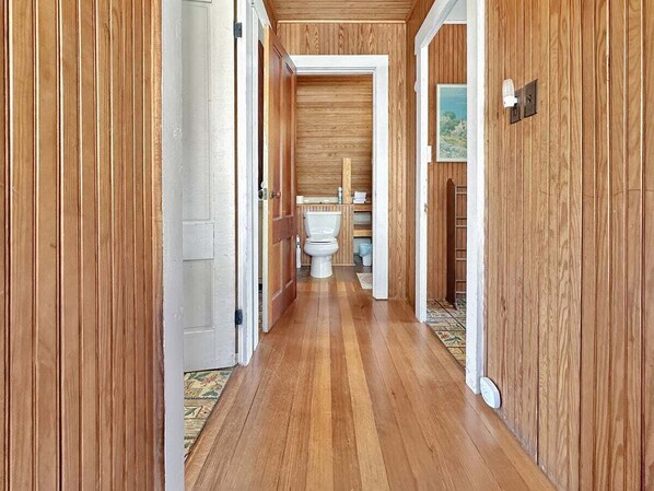 A wooden-paneled hallway with a toilet and a door leading to a room.