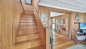 Un escalier en bois mène à une pièce où se trouvent une télévision, un fauteuil à bascule et un bureau.