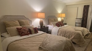Habitación de hotel con dos camas, cada una con colcha acolchada color beige y almohadas a juego. Se observan mesitas de noche con lámparas y objetos decorativos.