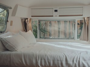 Un dormitorio con cama, cortinas y ventana con vista a palmeras.