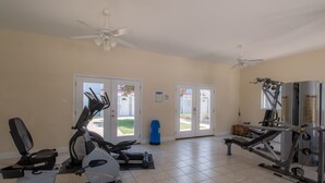 Et fitnessrum med træningsudstyr, ventilatorer i loftet og udsigt gennem glasdøre.
