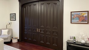 A large, dark wooden door with decorative panels, a framed picture of a horse race on the wall, a sofa with a patterned cushion, and a small table with a vase and a bottle. - Condo directly on Broadway!  Location, location, location!!  Walk to everything! (Saratoga Springs)