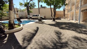 A courtyard with a swimming pool, a white pickup truck, and a building with balconies.