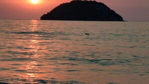 A sunset over a calm sea with a small island in the distance.