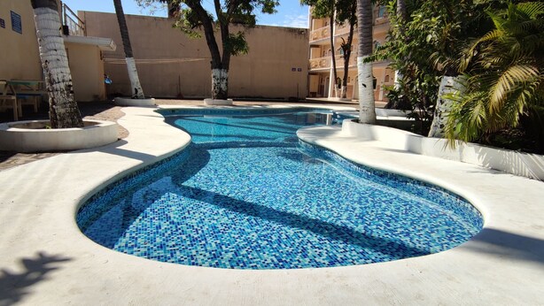 A swimming pool with a mosaic tile design, surrounded by palm trees and benches.