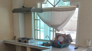 A kitchen with a gas stove, a sink, and a window with a view of the outside. There are two bar stools and a basket of dishes.