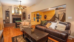 A cozy living room with a fireplace, leather sofa, and a ceiling fan.