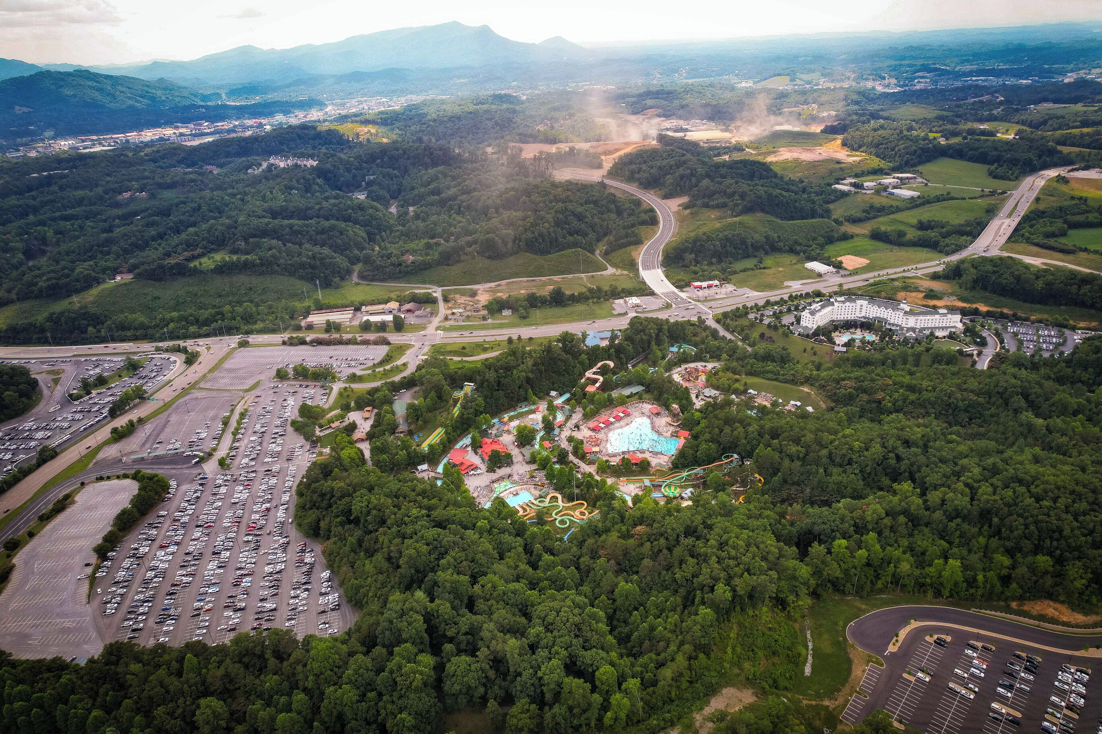 Vue aérienne d’un grand parking, avec un hôtel et un complexe de piscines.