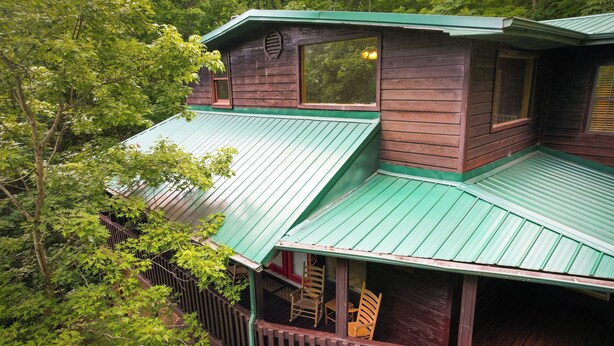 A cabin with a green metal roof, wooden walls, and a porch with wooden chairs.