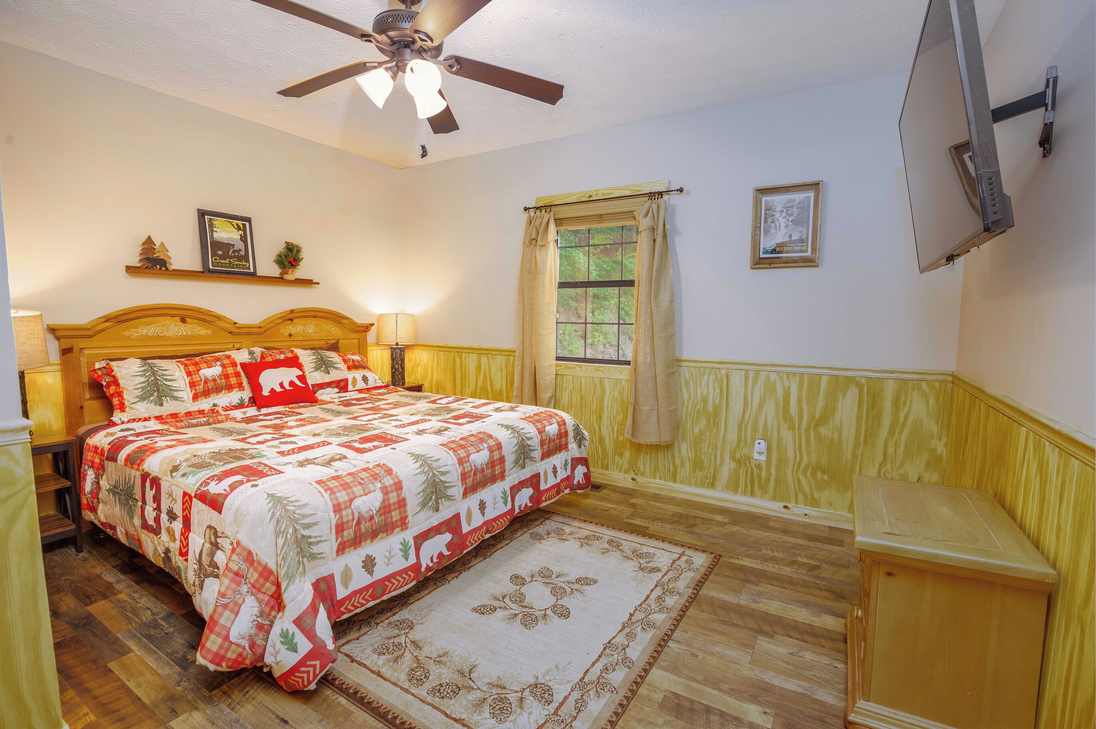 Un dormitorio con una cama de madera, ventilador de techo, ventana con cortinas y una mesita de noche de madera.