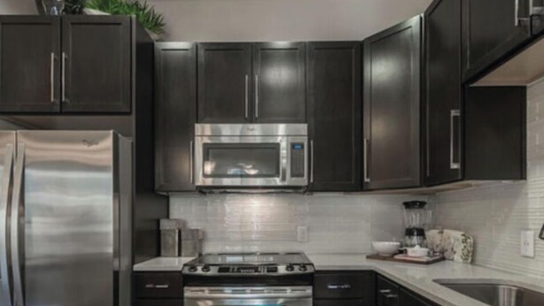 A modern kitchen with dark cabinets, stainless steel appliances including a refrigerator, microwave, and oven, and a white countertop. - City centre Apartment/Energy Corridor (Houston)