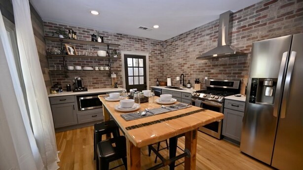 A modern kitchen with a brick wall, stainless steel appliances, and a wooden dining table set for four. - Backstage Gallery House (Decatur)
