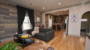 A living room with a grey sofa, a coffee table with toys, a wooden floor, and a kitchen in the background. - Backstage Gallery House (Decatur)