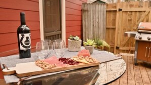 A glass table with a charcuterie board, a bottle of wine, and a grill in the background. - Backstage Gallery House (Decatur)