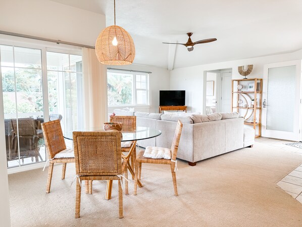 A spacious living room with a glass dining table, wicker chairs, a grey sofa, and a ceiling fan. - Paradise! Plantation at Princeville 3 Bed 3 Bath Condo (Princeville)