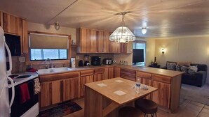 A compact kitchen with wooden cabinets, a central island, bar stools, a sink, and a chandelier. - Cozy cabin in a peaceful place (Ruidoso)