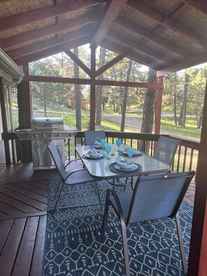A covered outdoor dining area with a grill, tables, and chairs.