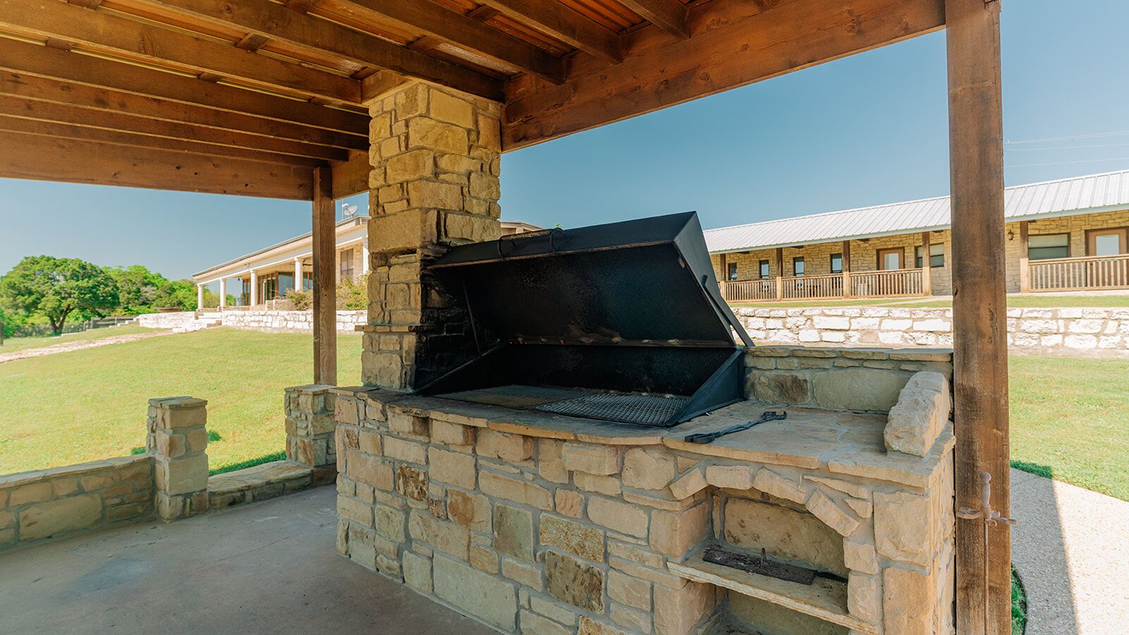 An outdoor stone barbecue grill under a wooden pergola.