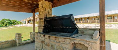 An outdoor stone barbecue grill under a wooden pergola.