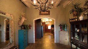 A lobby with a chandelier, a mounted deer head, a wooden cabinet, and a cow hide rug. - Cedar Creek Ranch on Lake Whitney (Whitney)