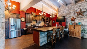 A modern kitchen with a central island, stainless steel appliances, wooden cabinets, and a brick accent wall. - Cedar Creek Ranch on Lake Whitney (Whitney)