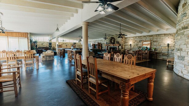 A spacious dining area with a long wooden table and chairs, surrounded by stone walls and a high ceiling with exposed beams. - Cedar Creek Ranch on Lake Whitney (Whitney)