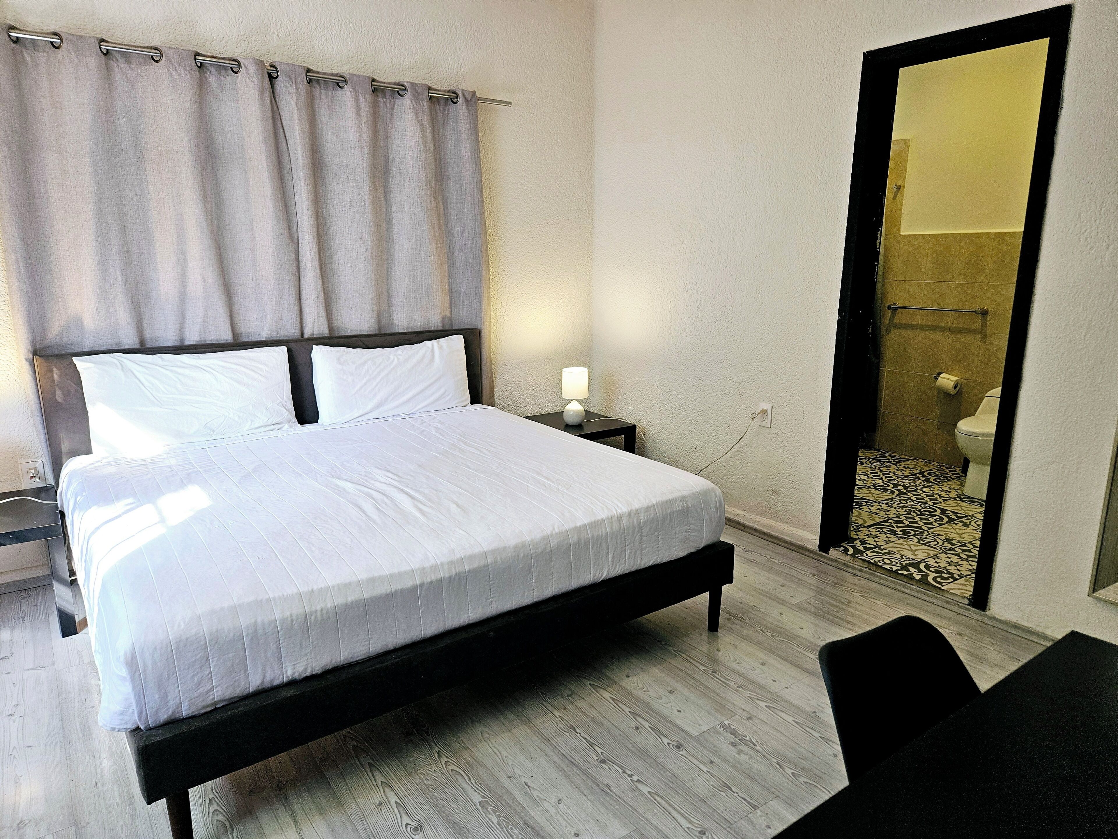 Une chambre à coucher avec un lit, une table de chevet et un miroir qui reflète une salle de bain.