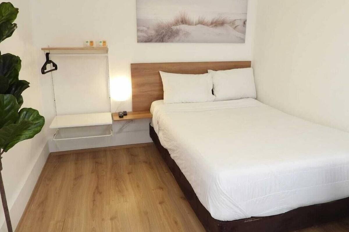 Une chambre à coucher avec un lit en bois, une table de chevet, une commode, une étagère fixée au mur et une grande plante.