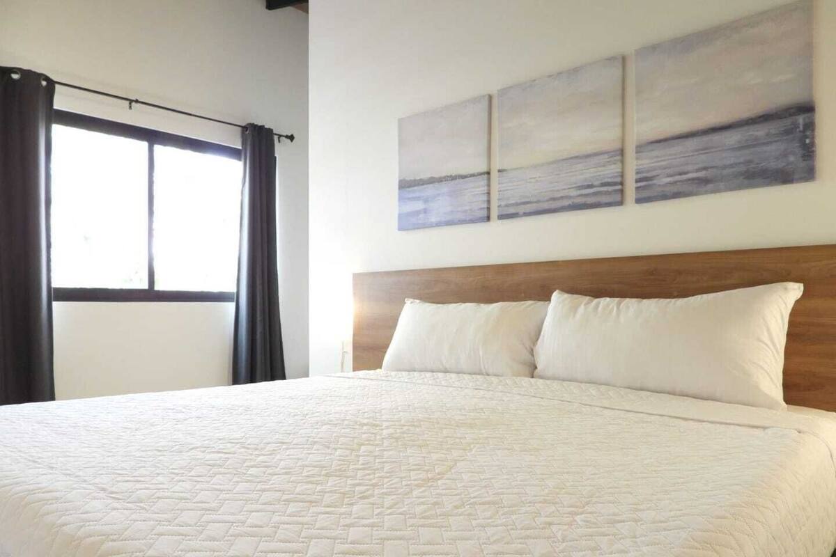 Une chambre d’hôtel avec un grand lit, une tête de lit en bois et trois tableaux accrochés au mur.