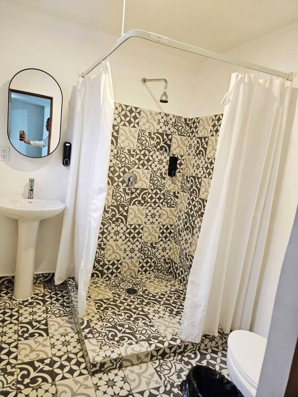 A bathroom with a shower, a sink, a mirror, and patterned tiles.
