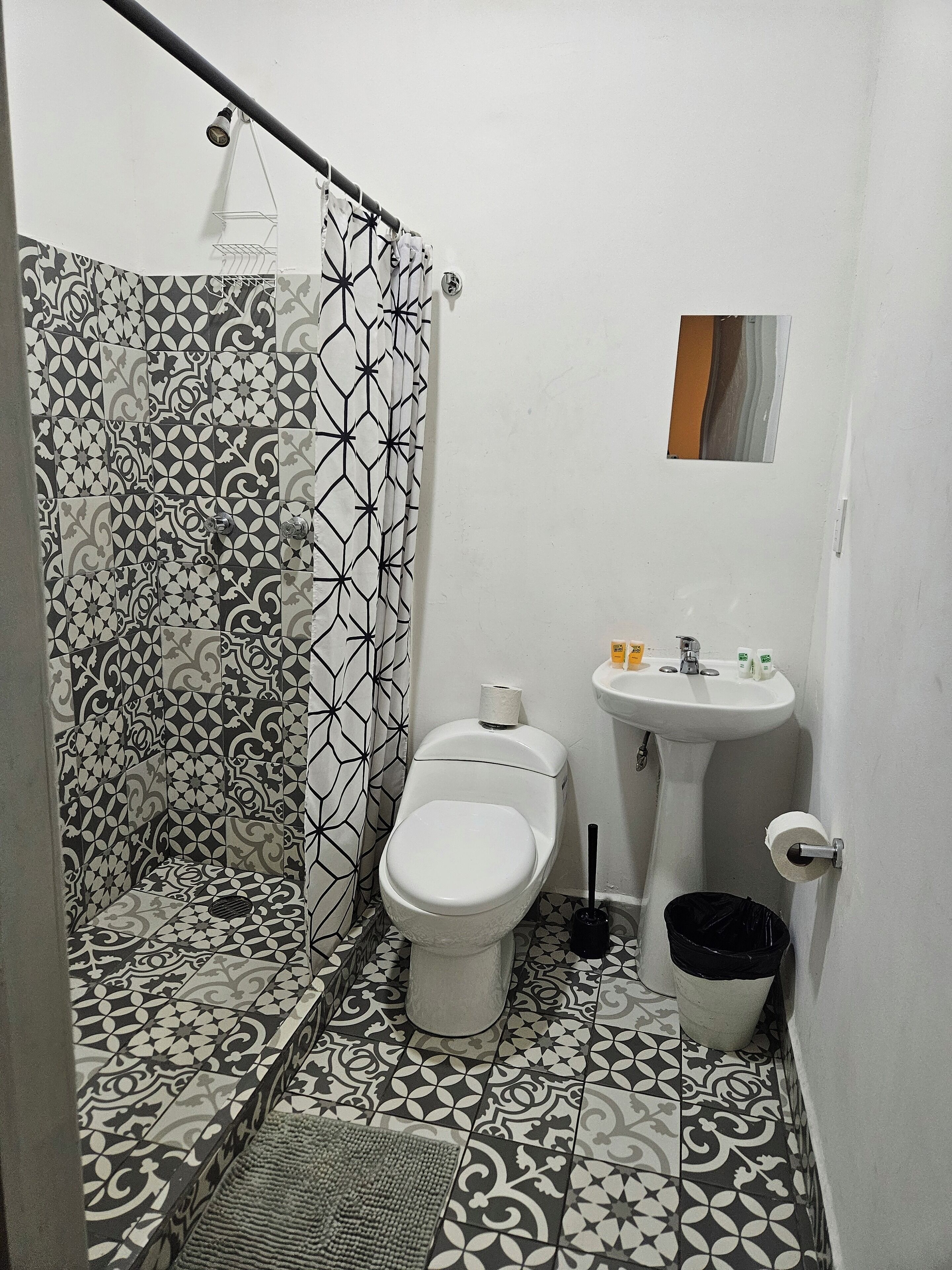 Een badkamer met betegelde vloer, toilet, wastafel, douchegordijn en een prullenbak.