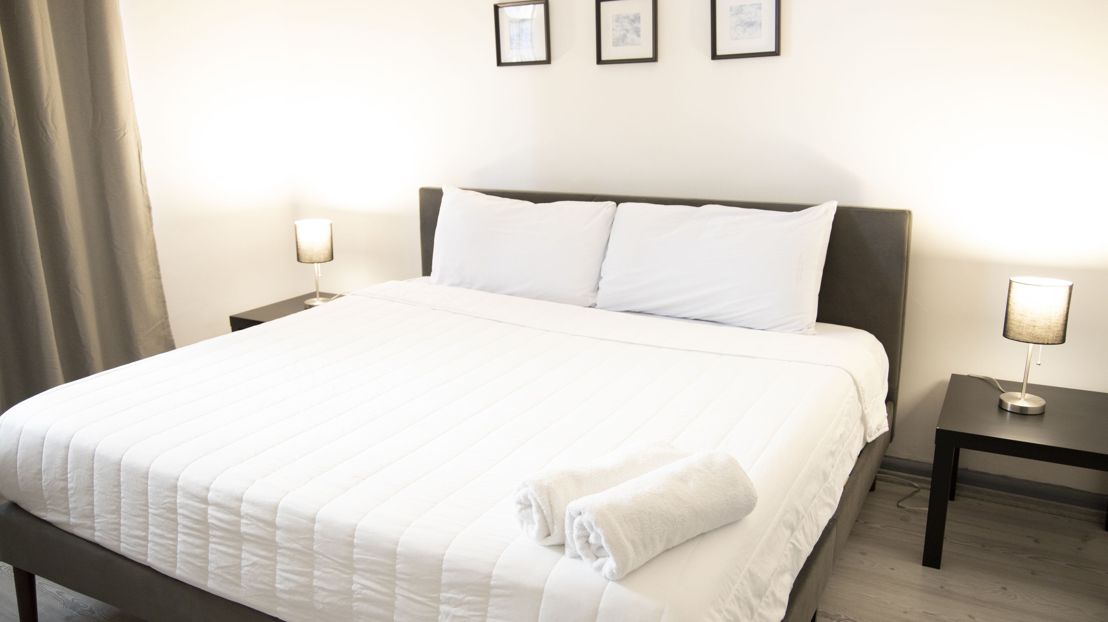 A neatly made bed with white bedding, two bedside lamps, and a framed picture on the wall.
