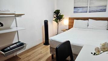 Habitación de hotel con cama, escritorio, silla, planta y obras de arte en la pared.
