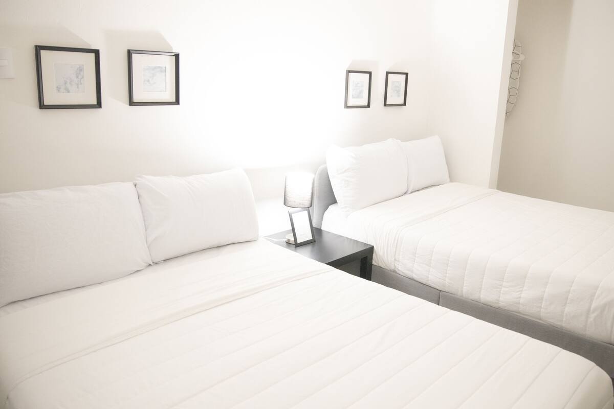 Une chambre d’hôtel avec deux lits, une table de chevet et une lampe fixée au mur.