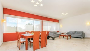 Een ruime woonkamer met een eethoek, grote ramen en een grijze bank.