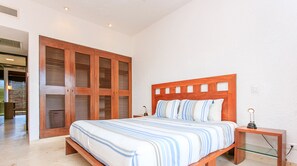 Een slaapkamer met een houten bed, strepenbeddengoed, een nachtkastje en een glazen plank.