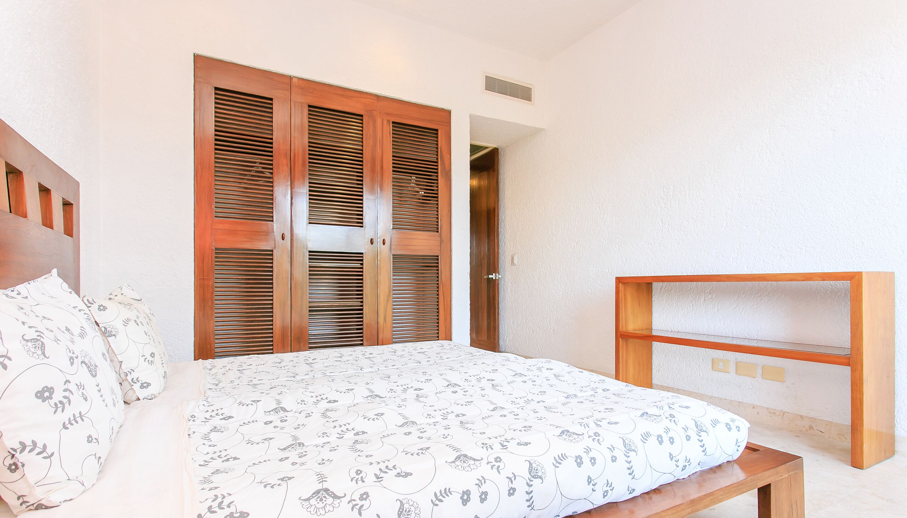 A bedroom with a bed, a wooden wardrobe, and a built-in shelf.